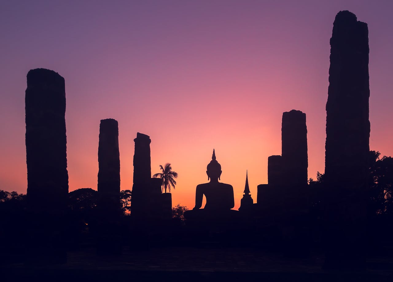 Tranquil silhouette of a Buddha statue at sunset in Sukhothai Historical Park, Thailand.